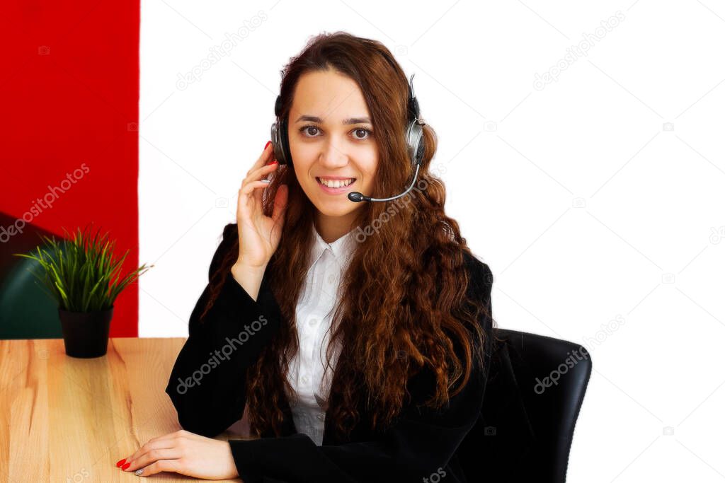 Portrait of a young woman employee of a call center of a real estate agency. Realtor in headphones with a microphone looks into the frame and smiles.