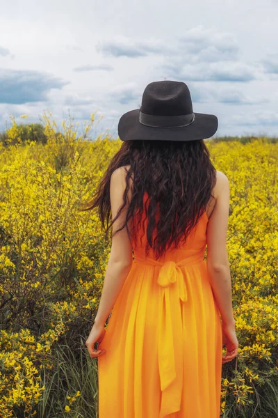 Girl from the back in a beautiful field of yellow flowers. Woman in a hat in a field from the back in summer with flowers.