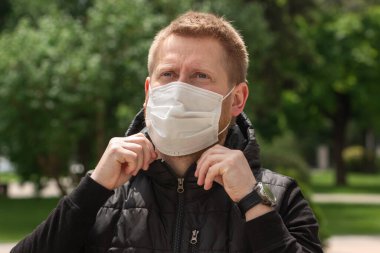 Yeşillik arka planında tıbbi maskeli bir adamın büyük portresi.