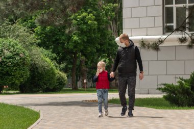 Babası ve maskeli küçük kızı parkta yürüyorlar.