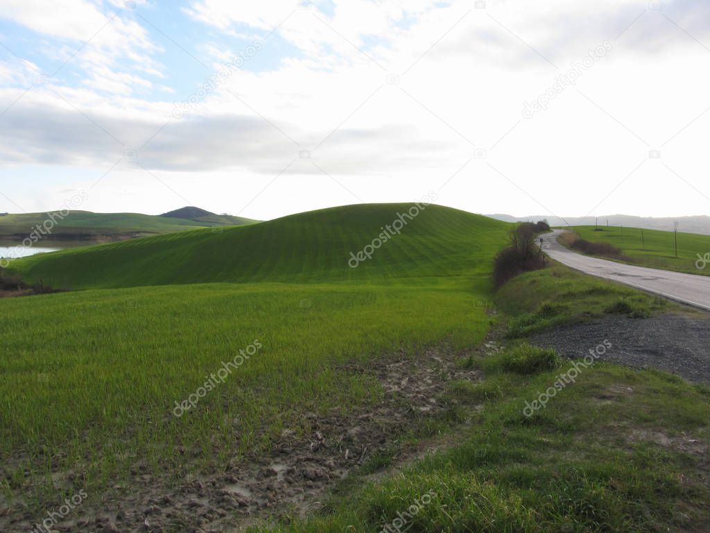 Country road over rolling green hills and valleys in winter . Tuscany, Italy