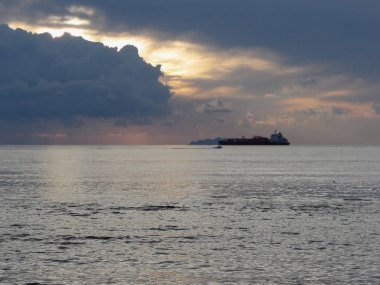 Kargo gemisi ve ufukta küçük bir balıkçı teknesi ile sıcak deniz gün batımı . Devler kümülonimbus bulutları gökyüzünde. Toskana, İtalya