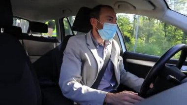 Ofisinin otoparkına girerken maske takan yetişkin bir iş adamı arabasını kullanıyor.