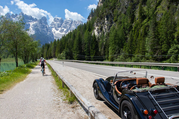 A vintage car with the italian dolomites mountain in the background. The classic car was having a tour during a summer holiday. Concept for tourism with style and road trip