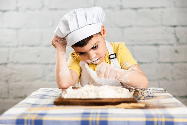 帽子を被った男の子とパン屋のエプロンは小麦粉を手で握っていて口と顔は汚れています 素朴な空気のシーン ライフスタイルパン屋 パンを作るために小麦粉を編む — ストック写真