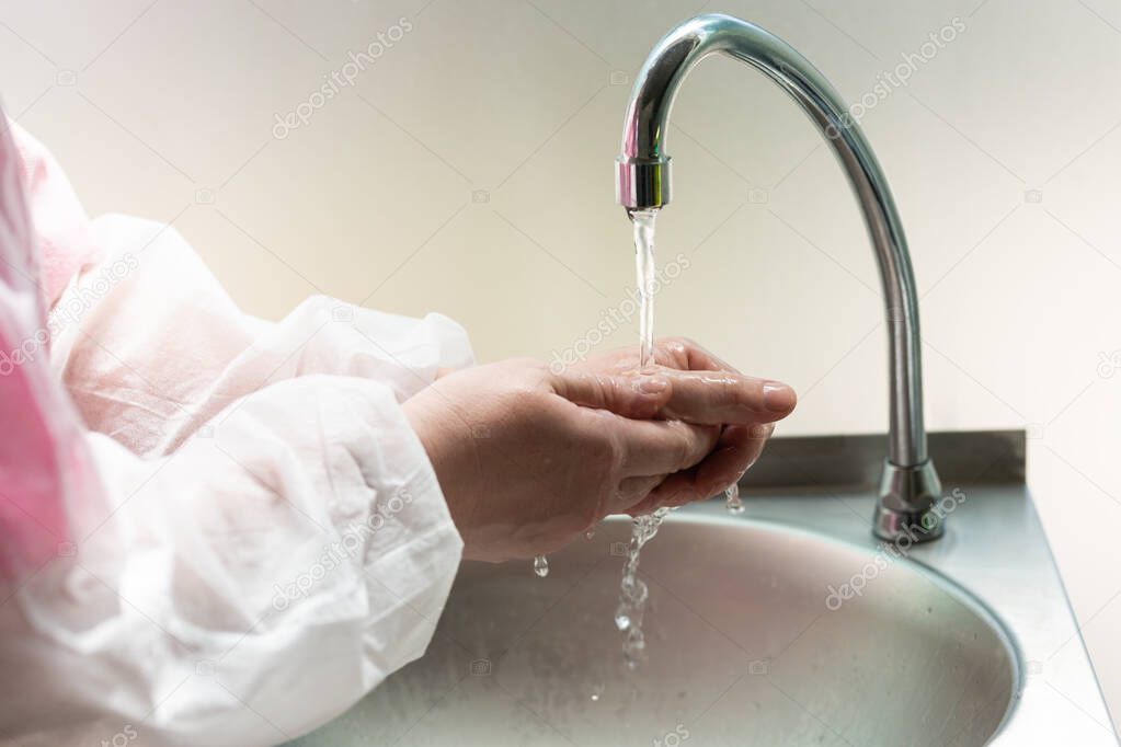 2 women's hands wash in water, disinfect coronavirus. hospital tap, clinical center. white protective suit (medical gown). new post-conoravirus normality. covid-19. Public health fighting epidemics