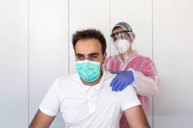 Kadın bir fizyoterapist erkek bir müşterinin göğsüne masaj yapıyor. Kovid-19 'u önlemek için pembe ve beyaz koruyucu giysiler, maske ve lateks eldivenler giyiyor. salgın virüsü.