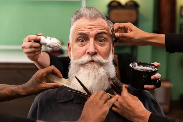 Mature man with white beard looking at camera in barber shop with barber hands with cutting and shaving instruments, brush, scissors, comb, razor. hipster style — Stock Image Mature Man White Beard Looking Camera Barber Shop Barber Hands Stock Photo