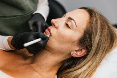 Bir güzellik kliniğinde ruj tasarımı yapmak için müşterilerin dudaklarında mikro pigmentasyon için profesyonel iplik işaretleme