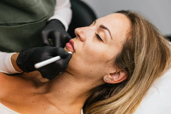 Bir güzellik kliniğinde ruj tasarımı yapmak için müşterilerin dudaklarında mikro pigmentasyon için profesyonel iplik işaretleme