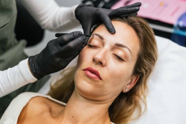 Güzellik salonundaki mikroplu patinaj işleminden önce kadın bir müşteriye iplik iziyle kaş tasarımı yapan estetikçi.