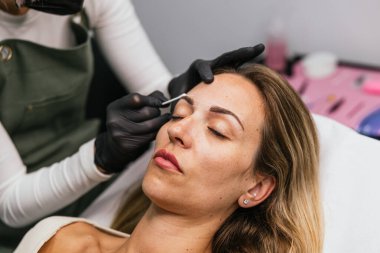 Güzellik teknisyeni, mikro patinaj yapmadan önce müşterinin kaşlarını şekillendirir. Kaş makyajı için kusursuz bir simetri sağlar.