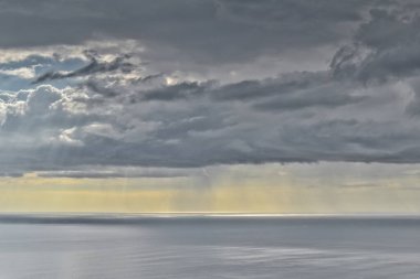 Güneş Tazman deniz ufkunda yağmur bulutları arasında parlıyor.