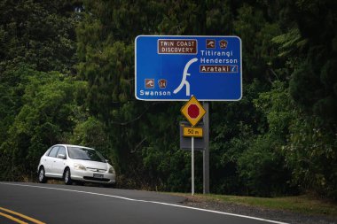 Auckland / New Zealand - February 8 2020: View of blue information road sign at Twin Coast Discovery route showing directions to Titirangi, Henderson and Swanson clipart