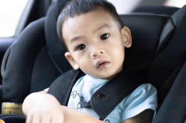 1 yaşında sevimli, Asyalı bir çocuk, kameraya bakarak araba koltuğunda oturan bir çocuk. Aile Gezileri ve Bebek Bakımı ve Güvenlik Konsepti. Ön Görünüm Kapalı Arkaplan Bulanık.