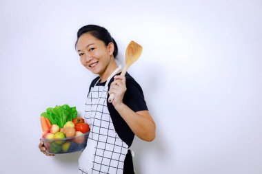 Asyalı Kadın Ayakta Gülümseme ve Karışık Taze Sebze Kutusu. Ev Yemekleri ve Ev İşleri Konsepti. Ayrı bir Beyaz Arkaplan ile Kapalı Kapılar Arkaplan Görünümünü Kopyala.