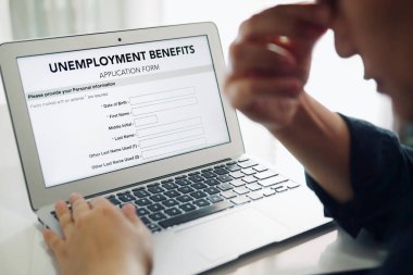 Unemployed depressed person filling out an online unemployment benefits application form using laptop computer. clipart