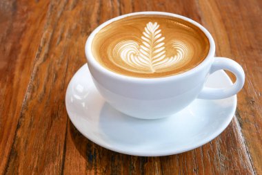 Sıcak kahve, latte cappuccino fincanı güzel 'rosetta' latte sanat sütlü köpüklü, ahşap masa zemininde..