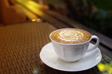 Sıcak kahve, karamelli macchiato cappuccino fincanı. Bahçe örtüsü, örülmüş sehpa sehpası. Ilık sabah güneşi, sığ alan derinliği..