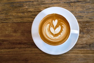 Sıcak kahve fincanının en üst görüntüsü Rosetta latte sanat sütlü, ahşap masa zemininde..