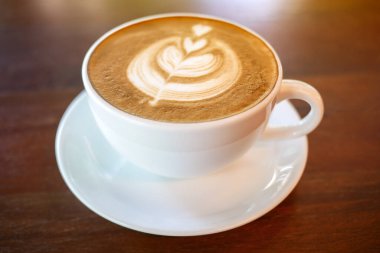 Sıcak kahve fincanı ahşap masa zemininde, sabah güneşiyle birlikte, sığ bir tarla derinliğinde..