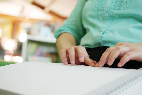 Close-up of blind person woman hands reading Braille book studying in creative library. Braille is a system of raised dots that can be read with the fingers by people who are blind or low vision.