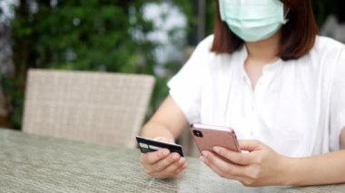 Maske takan bir kadın online ödeme yapıyor, internetten alışveriş yapıyor, Coronavirus COVID-19 salgınının ortasında kredi kartıyla yemek dağıtımı yapıyor. Nakitsiz finans ve online alışveriş kavramları.