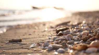 Mavi Bokeh doğa deniz plajı tropikal arka planda sabah güneşinde. Titreyen deniz dalgaları kumsala vurur deniz kabukları ve çakıl taşları güneş ışığına yansıyarak..