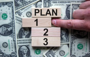 Tahta bloklar dolar banknotunun arka planında 1, 2, 3 kelimelerini oluşturur. Erkek eli. Güzel arka plan. İş konsepti.