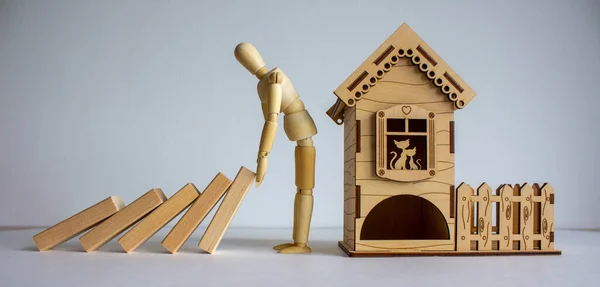 Wooden model of man stopping wooden domino blocks near wooden small house.