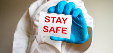 COVID-19 Pandemic Coronavirus konsepti. Sambo, jiu jitsu ve mavi tıbbi eldiven ve tıbbi maske takan diğer dövüş sanatları için beyaz kimonolu genç ve güçlü bir adam. Sözlü kart. Güvende kal..