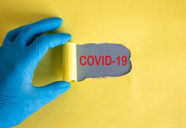 Yırtık sarı kağıdın arkasında beliren Covid-19 metni. Mavi eldiveni ver..