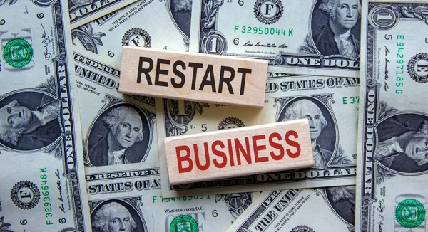 Concept words \'restart business\' on wooden blocks on a beautiful background from dollar bills. Business concept.