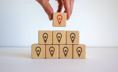 Erkek el, piramidin tepesine ampul işaretli bir küp yerleştiriyor. Beyaz masa. Güzel beyaz arka plan, kopyalama alanı. İş konsepti.