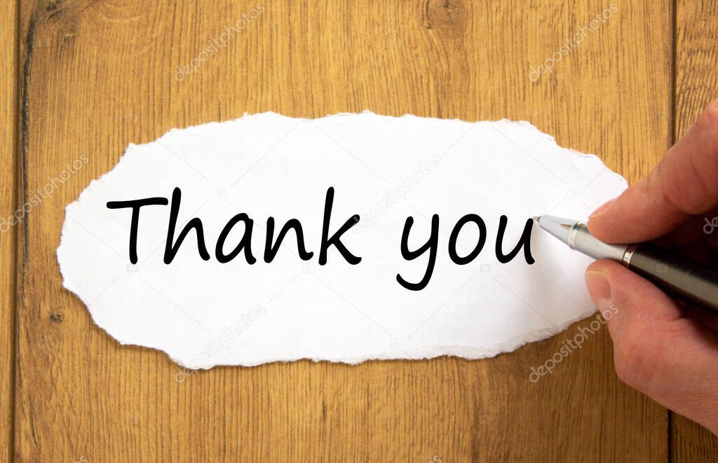 Male hand writing 'thank you' on white paper on wooden table. Business concept.