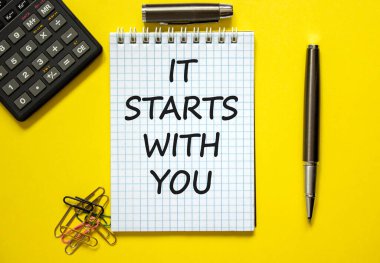 Güzel sarı arka plan, renkli ataçlar, metal kalem, kapak ve hesap makinesine 'seninle başlıyor' yazılı beyaz not. İş konsepti.