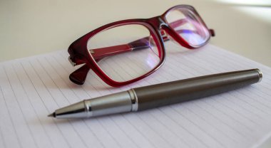 Beyaz nota üzerine metal kalem ve beyaz masada güzel gözlükler. İş konsepti.