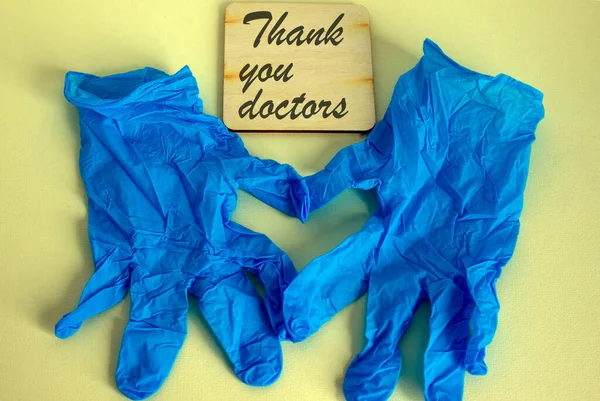 Blue medical gloves on yellow background folded in the shape of a heart. \