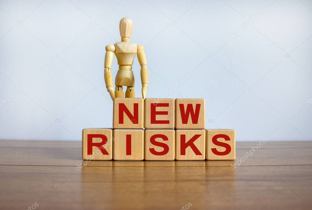 Concept words 'new risks' on cubes on a beautiful wooden table. Wooden model of human. Beautiful white background.