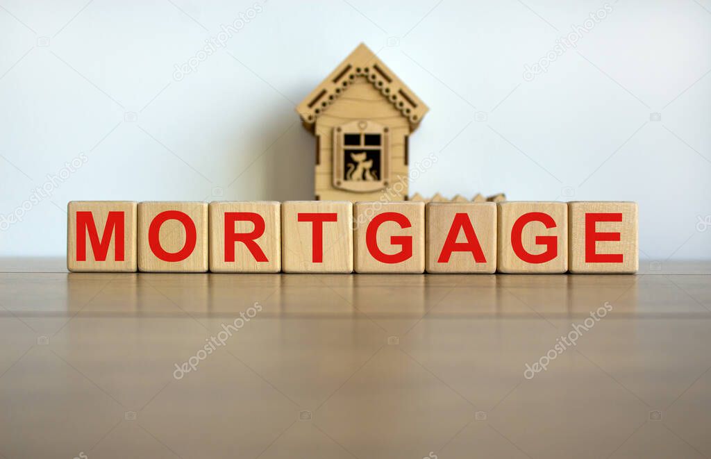 Wooden cubes form the word 'mortgage' near miniature house. Wooden table. Beautiful white background, copy space.