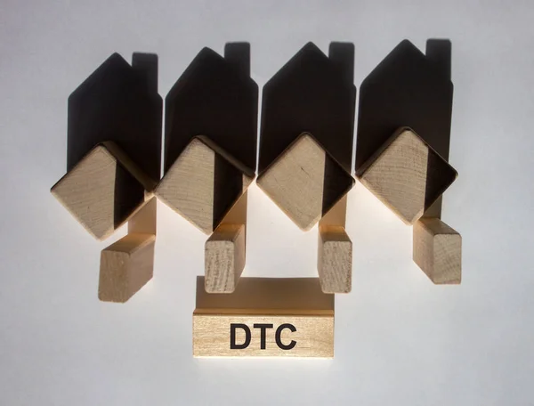 Houses created by shadows from wooden cubes. The word \'DTC\' on a wooden block. Direct to consumer concept. Beautiful white background.