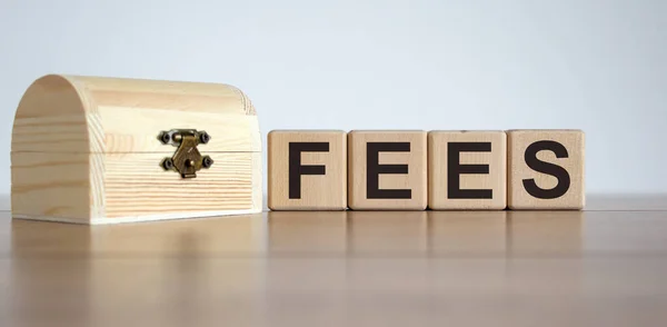 Cubes form the word \'fees\' near the wooden chest. Beautiful white background. Business concept. Copy space.