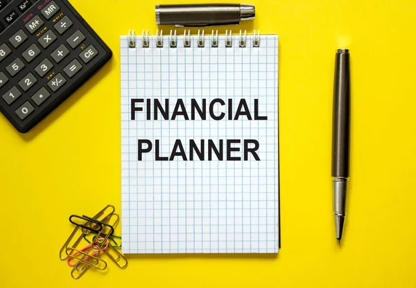 White note with inscription \'financial planner\' on beautiful yellow background, colored paper clips, metalic pen, cap and calculator. Business concept.