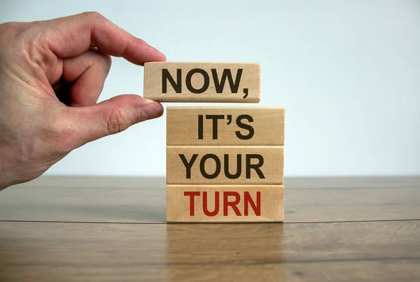 Wooden blocks form the words \'now, it\'s your turn\' on beautiful wooden table. White background. Male hand. Business concept.