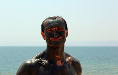 Çamura bulanmış gülümseyen adam, gözle görülür küçük deri parçaları. Ölü Deniz. Ürdün.