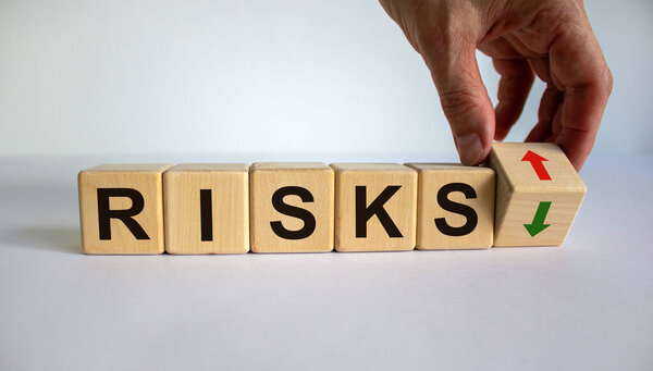 Hand is turning a cube and changes the direction of an arrow symbolizing that the risks is going down or vice versa. Beautiful white background, copy space. Business concept.