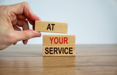 Erkek el blokların tepesine 'at' sözcüğüyle 'hizmetinizdeyim' sözcüğüyle bir blok yerleştiriyor. Güzel ahşap masa, beyaz arka plan. Uzayı kopyala İş konsepti.