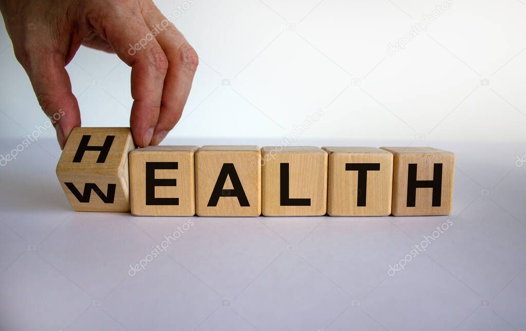 Hand is turning a cubes and changes the word 'health' to 'wealth' or vice versa. Beautiful white background, copy space. Business concept.