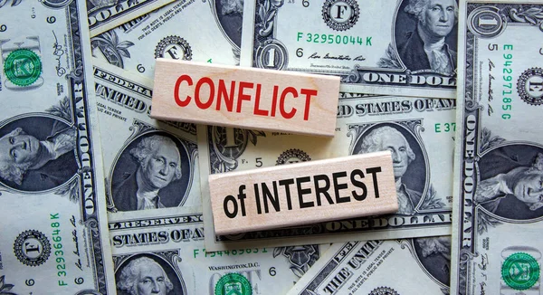 'Conflict of interest' words on wooden blocks. Business concept. Beautiful background from dollar bills. Copy space.