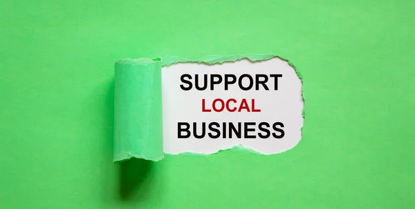 The text \'support local business\' appearing behind torn green paper. Business concept, copy space.
